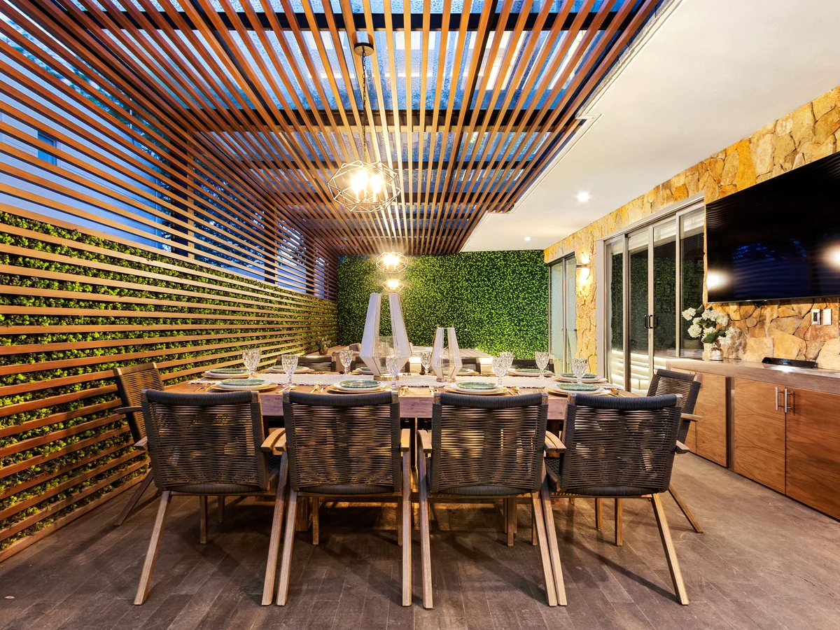 A62, private project: terrace with a wooden pergola, green wall and a lit outdoor dining area.