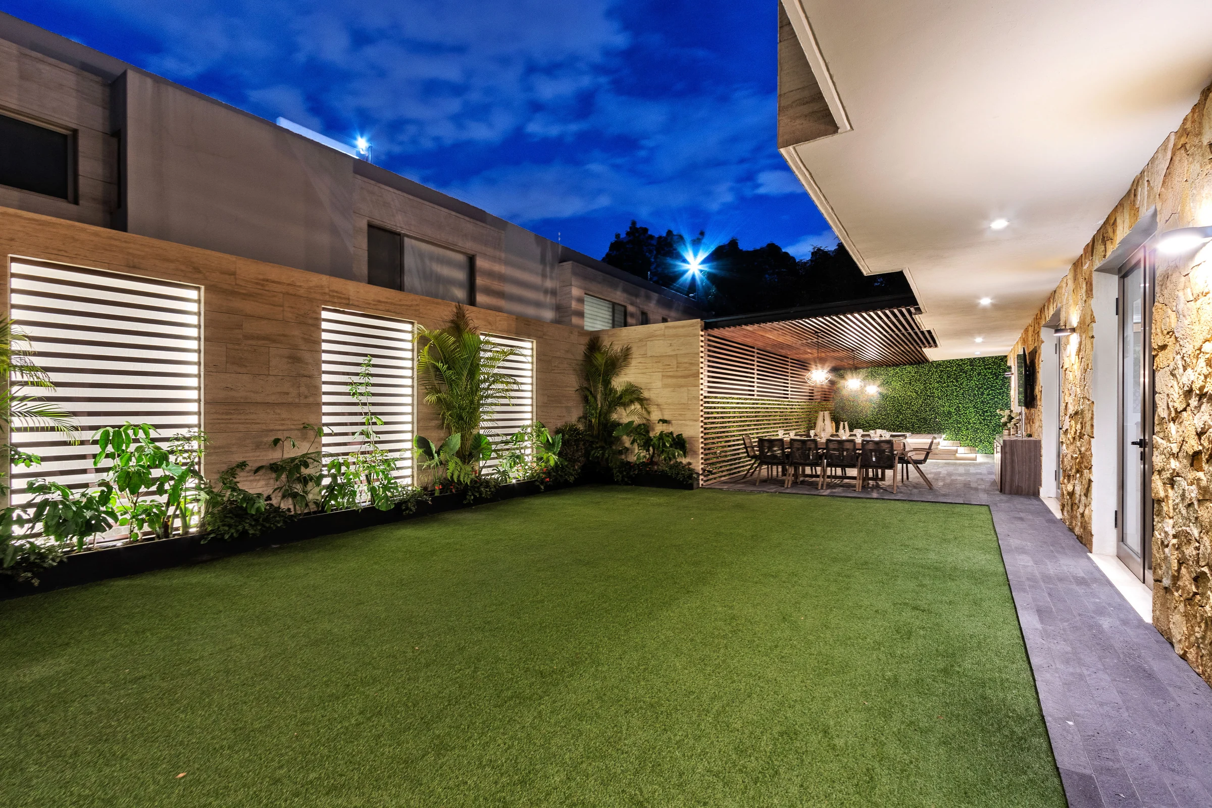 Garden of a delivered house at dusk, with illuminated lattices.