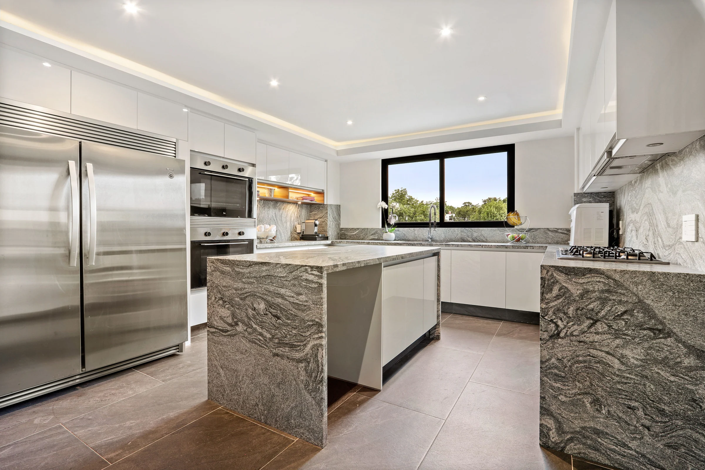 Finished kitchen with a granite island and countertops and white cabinets.